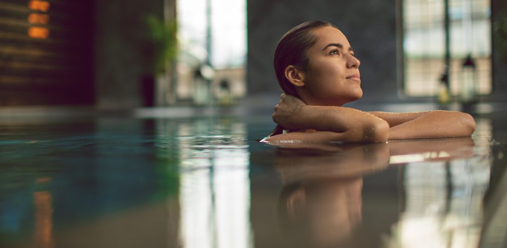 Belle jeune femme se relaxant au bord d'une piscine intérieure, se demandant que faire ce weekend à Paris